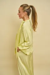 Blusa de satén color amarillo claro con escote en V y cuello de lazo ajustable. Presenta mangas largas holgadas con puños elásticos y diseño fluido.