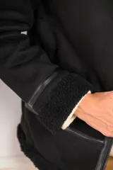Campera tipo gamulán de corte oversize, color negro, con interior y cuello de corderito sintético. Presenta cierre frontal, detalles de costuras y puños con terminación en corderito.