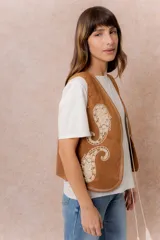 Chaleco corto de efecto gamuza en color tostado, con bordados decorativos en contraste y terminaciones bordadas en los bordes. Presenta escote en V y diseño recto.