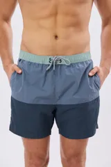 Short de baño con diseño de bloques de color en tonos celeste y azul marino, con cintura elástica en color verde claro y cordón ajustable.