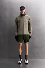 Camiseta relaxed fit de color verde militar, confeccionada en tejido con estructura waffle. Tiene cuello redondo, manga larga con puño elástico y un bolsillo plastrón con cierre de cremallera en el pecho.