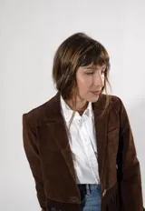 Blazer de gamuza color marrón con solapas clásicas, cierre frontal de un botón y detalle de flecos en el ruedo.