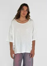 Remera de corte holgado color amarillo, con cuello redondo y mangas cortas con botones decorativos en los laterales.