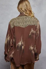 Chaqueta de algodón color marrón con diseño estilo patchwork, que incorpora parches con estampado animal print de leopardo en hombros y bolsillo frontal. Presenta detalles de tachas metálicas, bordes deshilachados, cierre frontal con botones metálicos y un acabado con efecto de pintura desgastada en las mangas.