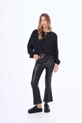 Blusa de satén color beige, con cuello redondo, detalle de volados en los hombros y cierre frontal con lazo. Presenta mangas largas con puños elásticos.