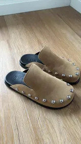 Zuecos color beige con tachas plateadas, base negra y plantilla con el logo de la marca.