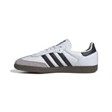 Championes Adidas Samba OG, color blanco con detalles en negro y gris. Diseño clásico de cuero con las tres tiras laterales en contraste y suela de goma marrón.