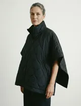 Poncho acolchado negro, con cuello alto y cierre frontal. Presenta un patrón de costuras circulares y bolsillos delanteros. Los laterales se ajustan con botones a presión.