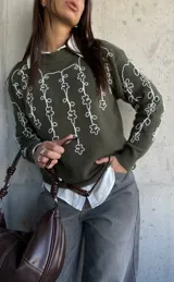 Sweater de punto color verde oliva con cuello redondo y diseño de flores bordadas en hilo blanco en el frente y las mangas.