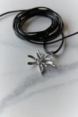 Collar con dije de acero quirúrgico en forma de flor de lirio, montado sobre un tiento de cuero encerado largo.