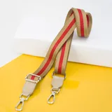 Correa de tela color beige con dos franjas rojas, con herrajes plateados y detalles en cuero sintético color beige.