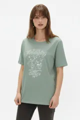 Remera de algodón blanca, de corte holgado, con cuello redondo y diseño estampado en el centro que incluye un gato comiendo de un plato y la inscripción 'Wild Cats'.