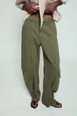 Pantalón cargo de tiro medio confeccionado en algodón, con diseño de pierna ancha y costuras verticales. Presenta bolsillos laterales y bolsillos tipo cargo con solapa en las piernas. El bajo es ajustable mediante trabillas con hebilla metálica.
