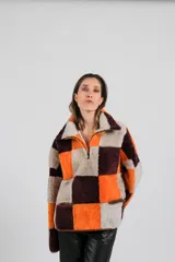 Buzo de cuero de oveja con diseño de bloques de colores en tonos naranja, bordó y beige. Presenta cuello alto con cierre frontal parcial, bolsillos laterales con cierre y textura de piel lanar.