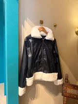 Campera negra de cuero sintético con cuello, puños y ruedo de corderito blanco.