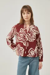 Camisa de poliéster con estampado floral en tonos bordó y crema, de corte holgado, cuello mao y cierre frontal con botones.