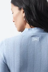 Polera de tejido de punto con textura calada y diseño de líneas verticales acanaladas. Presenta cuello alto y mangas largas con puños delicados, de silueta entallada.