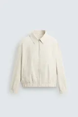 Cazadora de hombre color beige claro, de corte relajado, con cuello solapa, cierre frontal de cremallera y puños y bajo elásticos. Presenta una textura de rayas sutiles y efecto lavado.