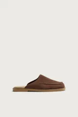 Zueco de piel con acabado serraje en color marrón, diseño sin talón, puntera redonda y detalle de costura tipo mocasín en el empeine.