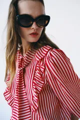 Camisa de manga larga con estampado de rayas rojas y blancas, cuello con lazo, volantes frontales y cierre de botones.