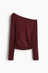 Remera de manga larga color bordó oscuro, con escote asimétrico de un solo hombro y frunces laterales que generan un efecto drapeado.