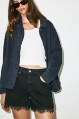 Shorts de denim negro de tiro alto con cinco bolsillos, cierre frontal con cremallera y botón, y detalle de encaje en el bajo.