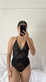 Body de encaje y microtul negro con diseño de escote halter, espalda descubierta y cierre con ganchos. Presenta paneles de encaje floral y secciones de tul transparente.