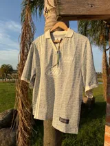 Polo de manga corta con cuello tipo polo y escote en V, corte boxy fit. Presenta un patrón texturizado en relieve y un logo ovalado con la inscripción "with love" en el pecho.