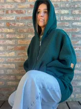 Campera de corderito color verde oscuro, con diseño holgado, cuello alto y manga larga. Presenta una etiqueta de cuero sintético en la manga.