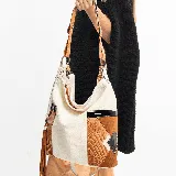 Cartera tipo hobo de cuero vacuno color crudo, con apliques de cuero texturizado color marrón y detalles en negro. Tiene correa de hombro corta y correa bandolera larga regulable y desmontable.