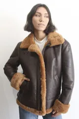 Campera bomber de cuero genuino color marrón oscuro, con interior y detalles en piel sintética color crema. Presenta cierre frontal, cuello solapa amplio y correas ajustables en el cuello y la cintura.