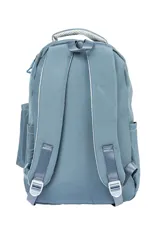 Mochila escolar de tela color azul claro, con múltiples compartimentos con cierre, bolsillo frontal con cierre y un pequeño accesorio colgante cilíndrico a juego. Presenta un parche circular con un emoji sonriente en el frente.