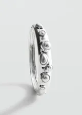 Pulsera rígida plateada con apliques de perlas y piedras incrustadas, y cierre metálico.