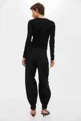 Pantalón negro de tiro medio con corte holgado y diseño de piernas globo, pinzas en la parte delantera y puños elásticos ajustados en los tobillos. Cuenta con cierre frontal y trabillas para cinturón.