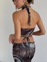 Top halter con estampado abstracto en tonos marrones y celestes, con abertura circular en el centro del pecho y lazos finos para atar en el cuello y la espalda.