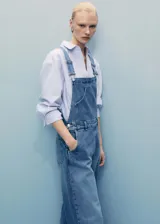 Jardinera de denim en color azul medio, con diseño de corte recto, tirantes ajustables con hebillas metálicas, cierre de botones laterales y bolsillos funcionales.