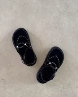 Sandalia de plataforma negra con tiras decoradas con tachas metálicas plateadas. Posee un diseño tipo ojota con ajuste de pulsera al tobillo mediante hebilla.