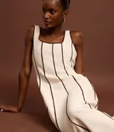 Vestido largo evasê sin mangas de color beige, con escote cuadrado y costuras verticales con bies en tono contrastante oscuro.