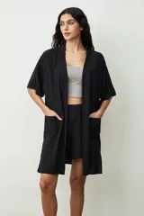 Camisa negra de manga corta, estilo kimono o bata ligera, con cuello solapa y bolsillos frontales amplios.