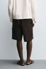 Bermuda de corte regular fit color marrón oscuro, confeccionada en tejido de lyocell y algodón. Presenta bolsillos cargo con solapa en las perneras, bolsillos delanteros y bolsillos traseros de vivo. Cierre frontal con cremallera y botón.