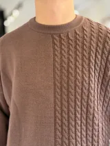 Sweater de punto oversize color marrón, con cuello redondo y diseño combinado: la mitad derecha cuenta con tejido de ochos y la izquierda es lisa. Incluye una etiqueta decorativa blanca en el frente inferior derecho.