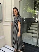 Vestido largo de tejido de punto con diseño de rayas verticales en blanco y negro. Presenta escote en V, mangas cortas y tajos laterales en el ruedo para mayor movimiento.