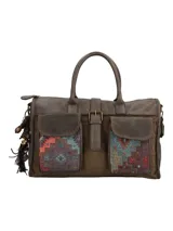 Cartera tipo bolso de mano y bandolera en color marrón, con diseño patchwork étnico en los bolsillos frontales. Cuenta con dos bolsillos exteriores con solapa y broche magnético, cierre principal con cremallera, manijas fijas y correa ajustable y removible. Incluye un llavero decorativo con borlas y dijes colgantes en el lateral.