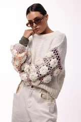 Sweater de punto con cuerpo liso en color negro y mangas largas tejidas en crochet gris con aplicaciones de flores en relieve color blanco.