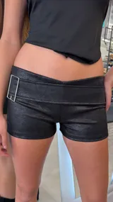 Short de tiro bajo confeccionado en cuerina de efecto texturizado y acabado brillante, color negro. Presenta una faja ancha cruzada en la cintura y hebilla metálica rectangular lateral.