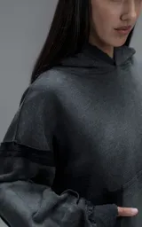 Hoodie oversize de corte crop en color gris oscuro con efecto desgastado. Presenta costuras expuestas, detalles de roturas en el ruedo y en la capucha, y bolsillos frontales con bordes reforzados.