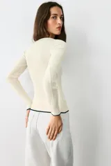 Chaqueta de punto marrón con cuello redondo, manga larga y ribetes en color rojo. Cuenta con cierre frontal de botones.