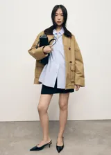 Anorak de estilo oversize en color tostado, con cuello camisero de pana en contraste. Presenta cierre frontal mediante ganchos metálicos y dos bolsillos de parche con solapa en la parte delantera.
