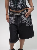 Bermuda de denim negro con bordados blancos estilo barroco/rococó en los bolsillos traseros y a lo largo de los costados. Presenta costuras contrastantes blancas, tiro medio y calce holgado (baggy fit). En la parte superior trasera lleva un aplique con el texto "Urban Coutur".