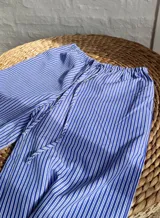 Pantalón palazzo celeste a rayas verticales blancas, de tiro alto y corte holgado.